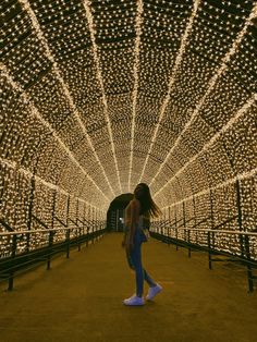 a woman is walking through a tunnel covered in lights