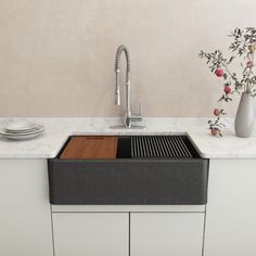 a kitchen sink sitting under a faucet next to a vase with flowers in it