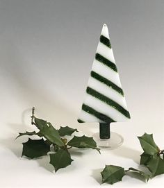 a small green and white christmas tree on a glass base with holly leaves around it