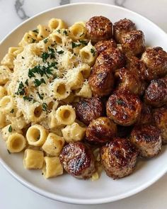 pasta with meatballs and parmesan cheese on a white plate sitting on a marble table