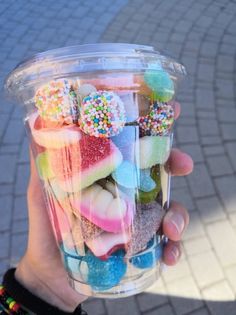 a person holding up a plastic cup filled with lots of candies and sprinkles