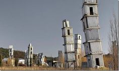 there are many tall metal structures in the middle of a grassy field with trees and buildings behind them