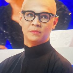 a man with bald hair wearing glasses and a black turtle neck shirt is looking at the camera