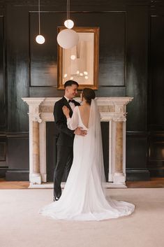 a bride and groom standing in front of a fireplace