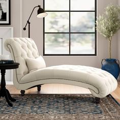 a white chaise lounge chair sitting on top of a rug in front of a window