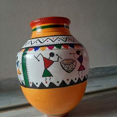 an orange and white vase sitting on top of a floor next to a wall with designs painted on it