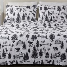 a bed covered in a white and black forest print comforter set with two pillows