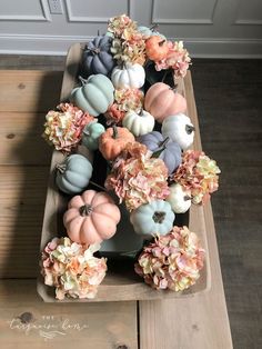 a wooden tray filled with lots of fake flowers and pumpkins on top of a table