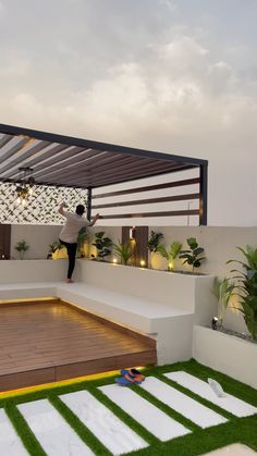 a man standing on top of a wooden deck next to a lush green yard and white walls