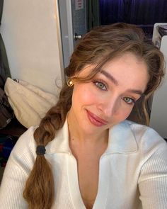 a woman with long hair wearing a white sweater and gold hoop earrings is smiling at the camera