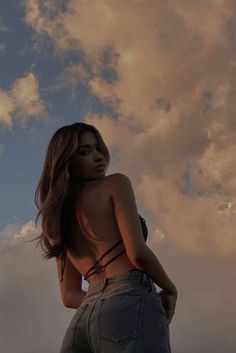 a woman standing in front of a cloudy sky with her back turned to the camera