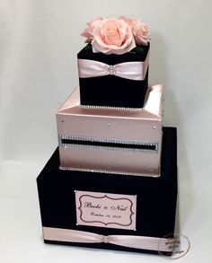 three tiered black and pink wedding cake with flowers on each tier, decorated with ribbon