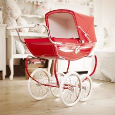 a red baby carriage sitting on top of a hard wood floor next to a white dresser