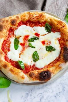 a small pizza on a plate with cheese and basil