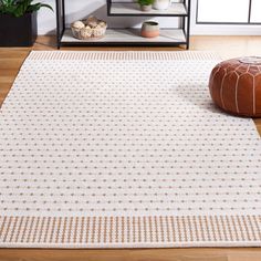 a white rug with brown dots on it in front of a book shelf and potted plant