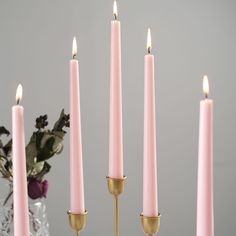 four pink candles are lined up in front of a vase with flowers and greenery