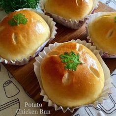 four rolls with green garnishes sitting on top of a wooden cutting board