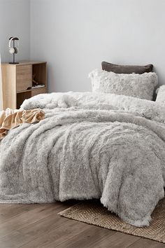 a bed covered in fluffy grey blankets and pillows