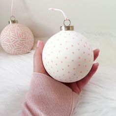 a woman's hand holding a white ball ornament with pink polka dots