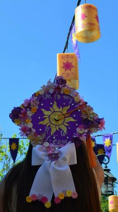 a woman wearing a purple hat with flowers on it's head and two candles hanging from the top