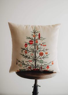 a christmas tree pillow on top of a wooden stand with a white background and red ornaments