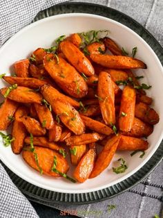 a white bowl filled with cooked carrots on top of a gray and white table cloth