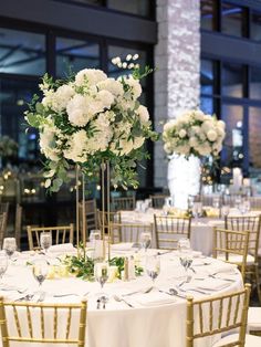 the tables are set up with white flowers and greenery in tall centerpieces