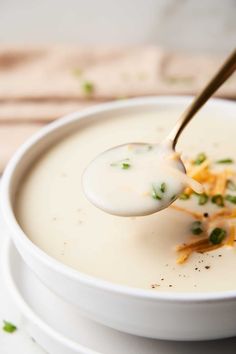 a spoonful of soup with cheese and chives on it in a white bowl