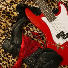 a red guitar and black booties are laying on a leopard print blanket