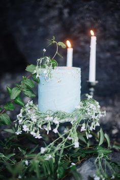 a blue cake sitting on top of a table next to two white candles and greenery