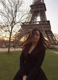 a woman is standing in front of the eiffel tower, looking at the camera