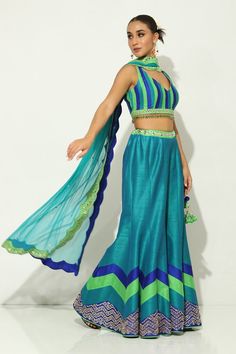 Peacock green and blue padded blouse with mirror work, tasseled hem and cutout details. Paired with a sharara with a mirror embroidered waistline and hem and dupatta with scallop embroidered dupatta. - Aza Fashions Green Art Silk Sharara With Unstitched Blouse, Green Chanderi Blouse For Party, Blue Chanderi Choli For Party, Blue Party Choli In Chanderi, Sleeveless Green Choli For Party, Green Art Silk Palazzo Set For Navratri, Green Chanderi Sharara For Party, Green Choli For Diwali, Sleeveless Green Sets For Reception