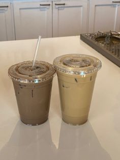 two iced coffees sitting on top of a counter next to each other in plastic cups