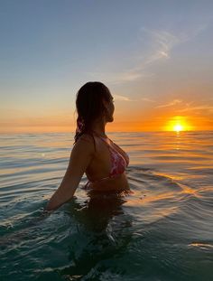 a woman is sitting in the water at sunset