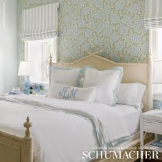 a white bed sitting in a bedroom next to a window covered in blue and white wallpaper