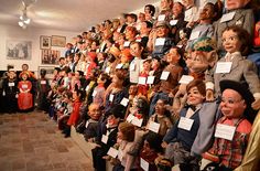 a large group of people standing next to each other in front of a wall full of dolls