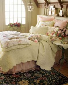 a bed with white comforter and pillows in a room next to a table filled with flowers