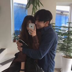 a man and woman taking a selfie in front of a window with their cell phone