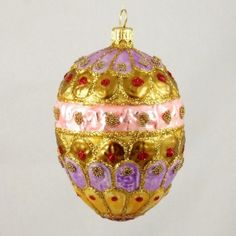 a gold ornament with pink and purple designs hanging from a chain on a white wall