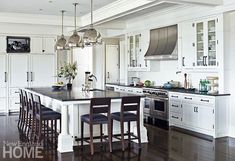 a large kitchen with white cabinets and black counter tops, an island in the middle is surrounded by bar stools