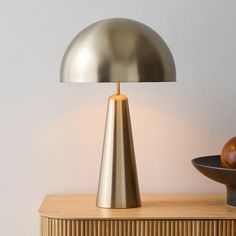 a table lamp sitting on top of a wooden cabinet next to an apple and bowl