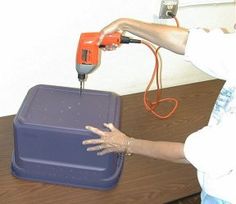 a woman using an electric drill to fix a blue box on a wooden table next to a white wall