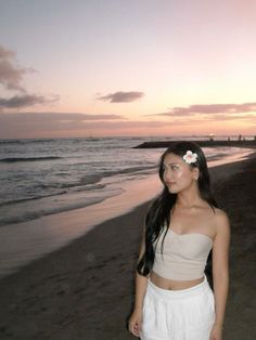 a woman standing on top of a sandy beach next to the ocean at sunset or dawn