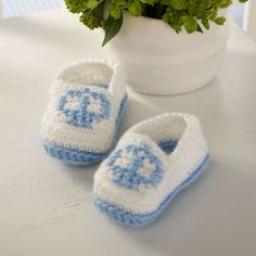 a crocheted blue and white baby booties next to a potted plant