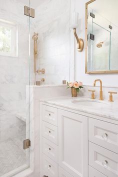 a white bathroom with marble counter tops and gold fixtures