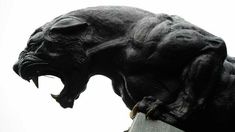 a statue of a black panther on top of a cement pillar with its mouth open