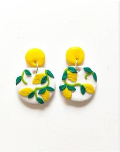 two yellow and white earrings with green leaves on the bottom one has a lemon in it