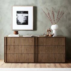 a wooden cabinet with two vases on top of it next to a framed photograph