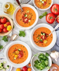 four bowls of tomato soup on a table with tomatoes, parsley and other vegetables