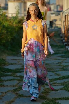 a woman walking down a sidewalk wearing a colorful dress and necklace with long hair in the wind